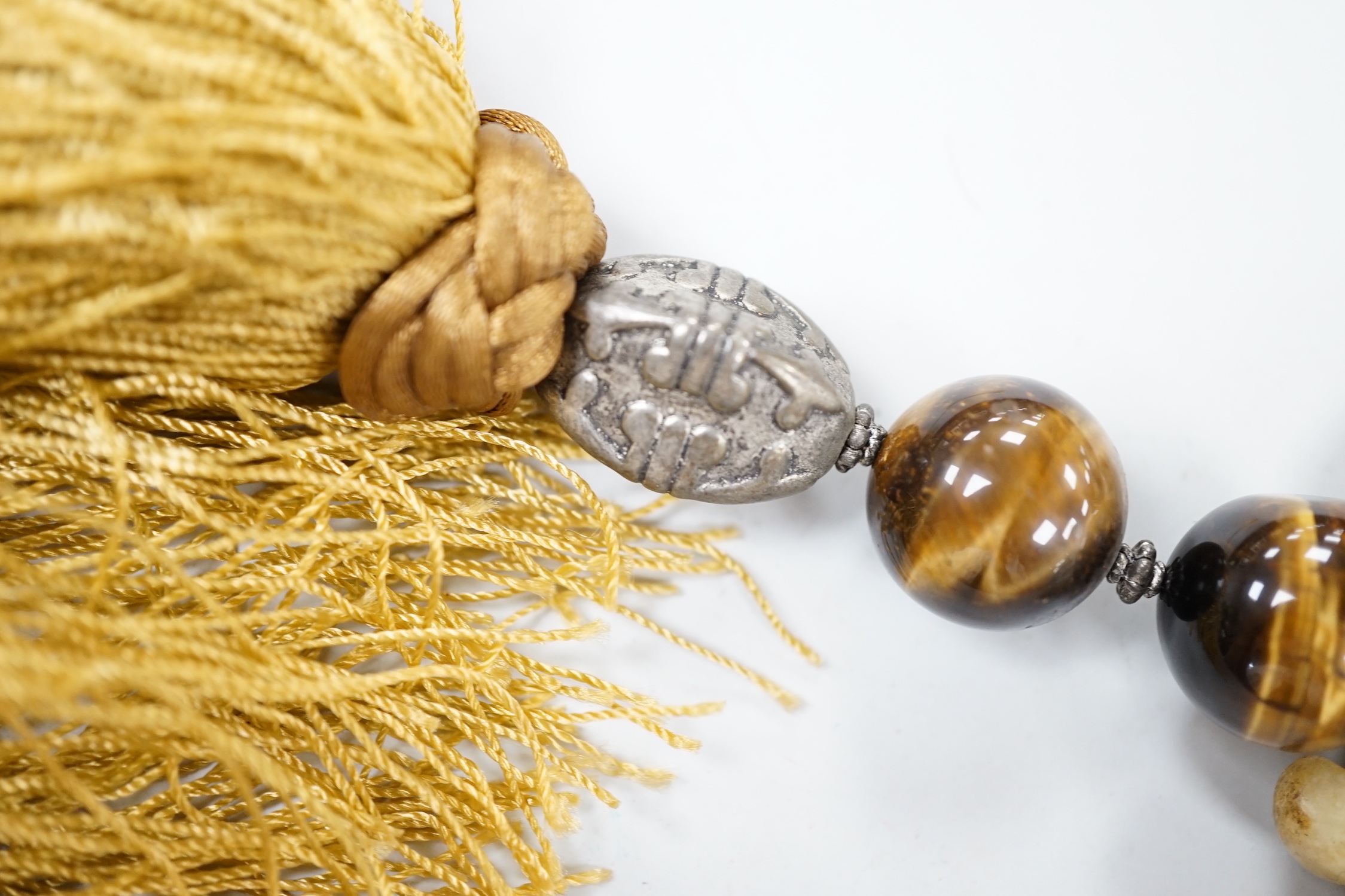 A large Chinese bowenite jade disc, threaded with tiger's eye beads and long silk tassel, 90cm long